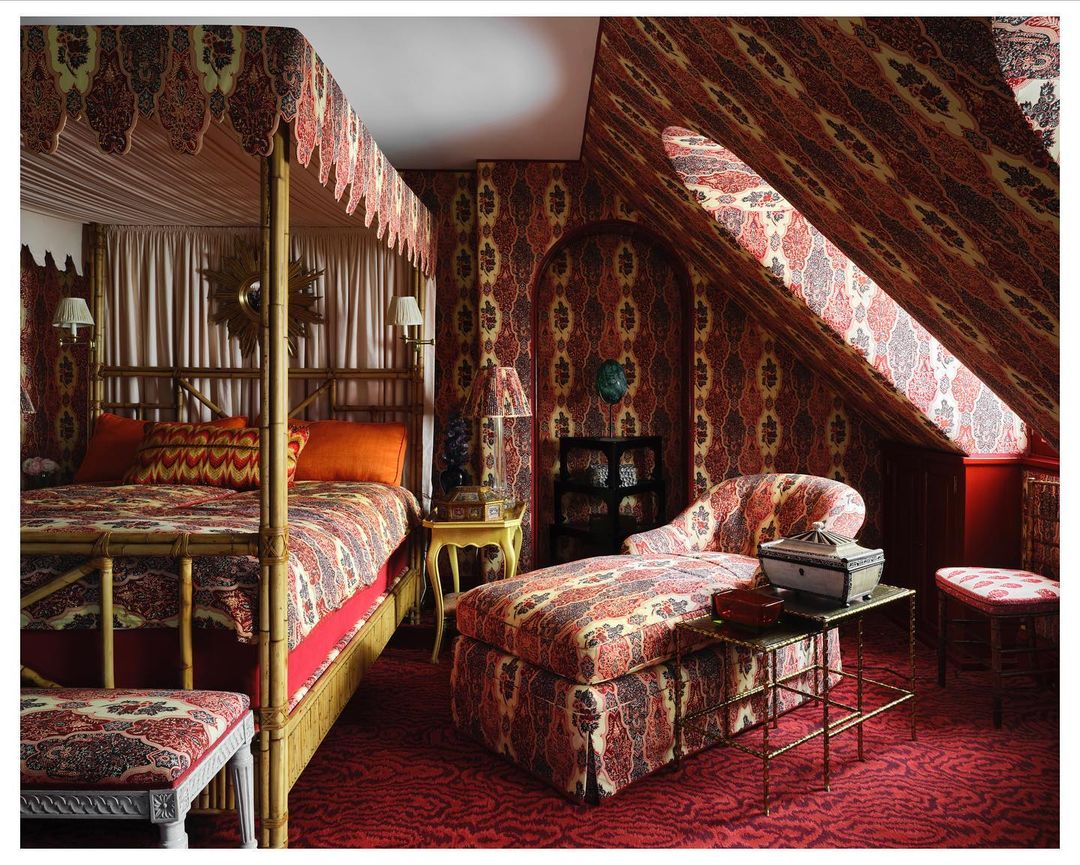 Luxurious bedroom features a four-poster bed, patterned chaise lounge, and walls covered in a coordinated ornate paisley fabric design.