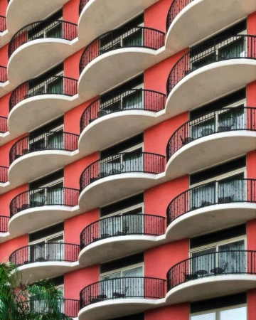 Exterior vertical architectural photograph of a salmon-colored hotel building with white balconies and black railings, bathed in light.