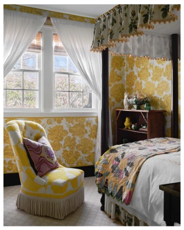 Bedroom interior featuring a wingback chair, four-poster bed, and floral wallpaper creating a cozy and decorative atmosphere.