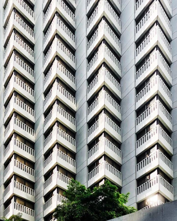 Exterior view of a tall building with multiple balconies that create a zig-zag pattern and small green trees at the base.