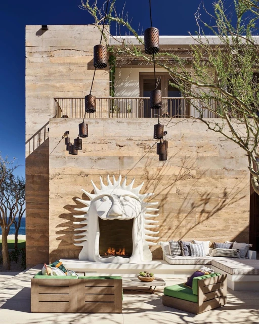 Outdoor patio area featuring a modern stone fireplace, comfortable seating, and architectural details against a blue sky and ocean backdrop.