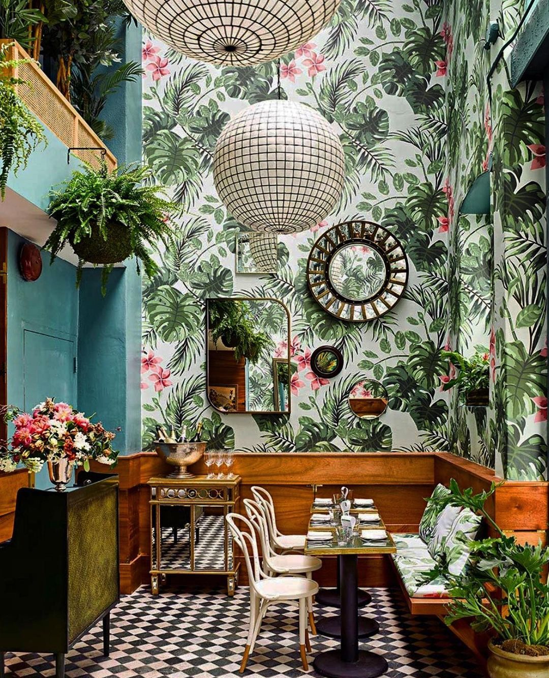 Indoor dining area with tropical leaf wallpaper, pendant lighting, wooden booths, and black-and-white checkered flooring creates a stylish ambiance.