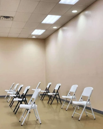Indoor shot of rows of black and white folding chairs on a beige floor, under fluorescent lights and against a beige wall.