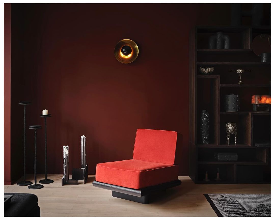 Red accent chair in a modern room with minimalist decor, warm lighting, and a red wall, creating a cozy and stylish interior.