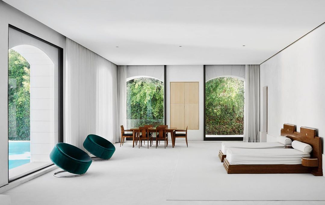 Bright, open architectural interior showcasing a dining area, lounge chairs near a pool view, and a sleeping area with twin beds.