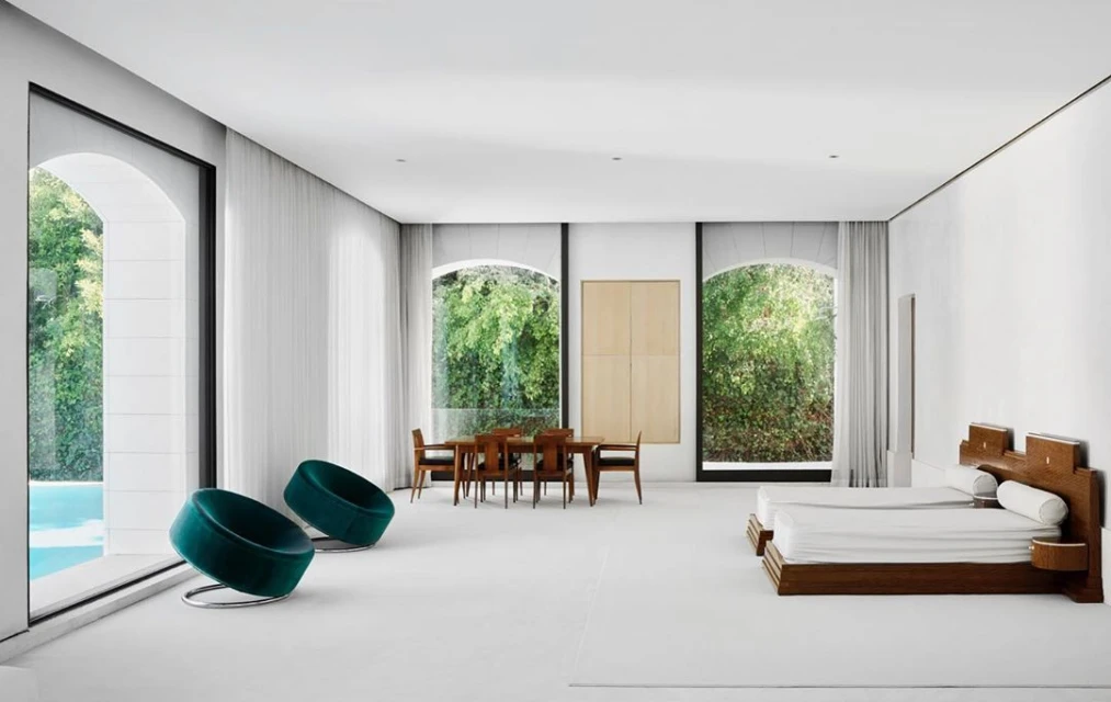 Bright, open architectural interior showcasing a dining area, lounge chairs near a pool view, and a sleeping area with twin beds.
