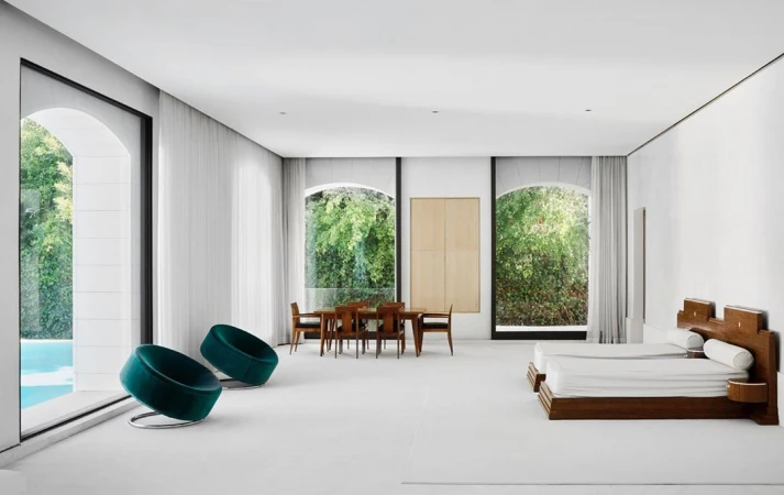 Bright, open architectural interior showcasing a dining area, lounge chairs near a pool view, and a sleeping area with twin beds.