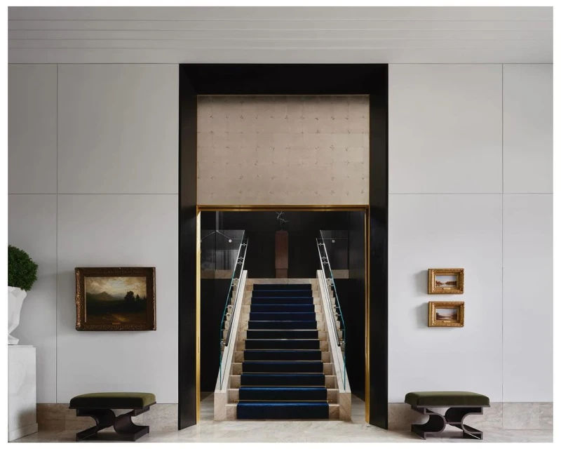 Interior design featuring a staircase with a blue carpet, framed artwork on the wall, and two benches in a bright, modern space.