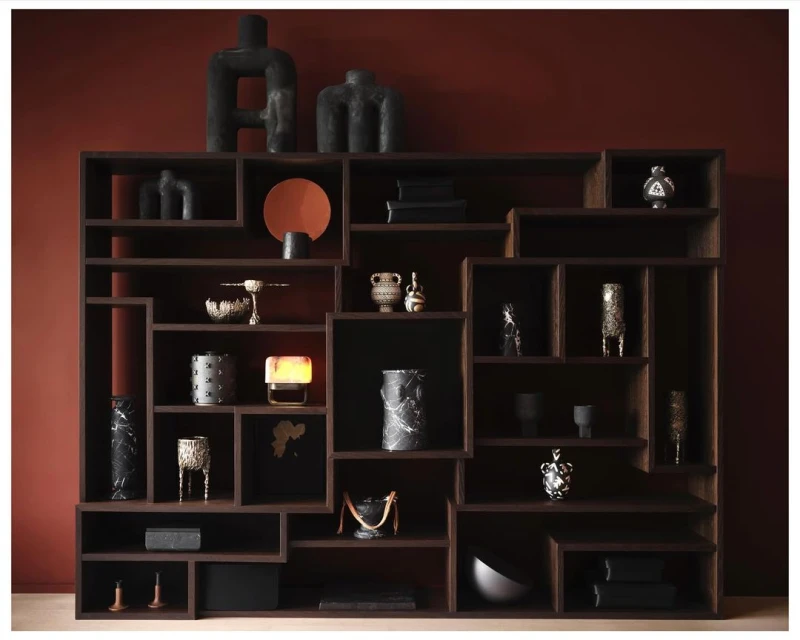 Interior view of a wooden bookcase with decorative objects against a dark red wall, creating a warm, inviting aesthetic.