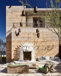 Sunny outdoor patio with a sculptural white sun fireplace, modern wooden lounge chairs, and hanging pendant lamps.
