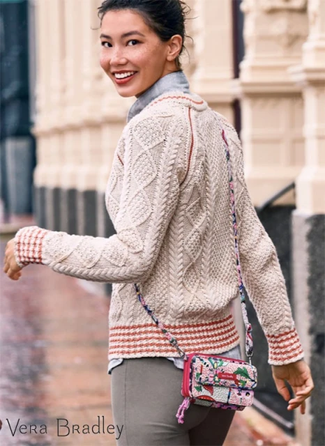 Smiling Asian woman in outdoor setting wearing a patterned cardigan, grey pants, and a floral Vera Bradley crossbody bag.