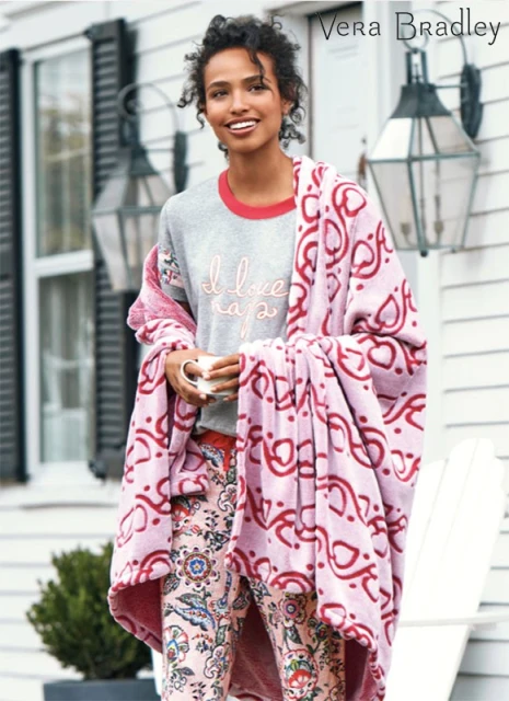Woman in pajamas and a blanket stands outside a white house with dark shutters, holding a mug in a Vera Bradley product shot.