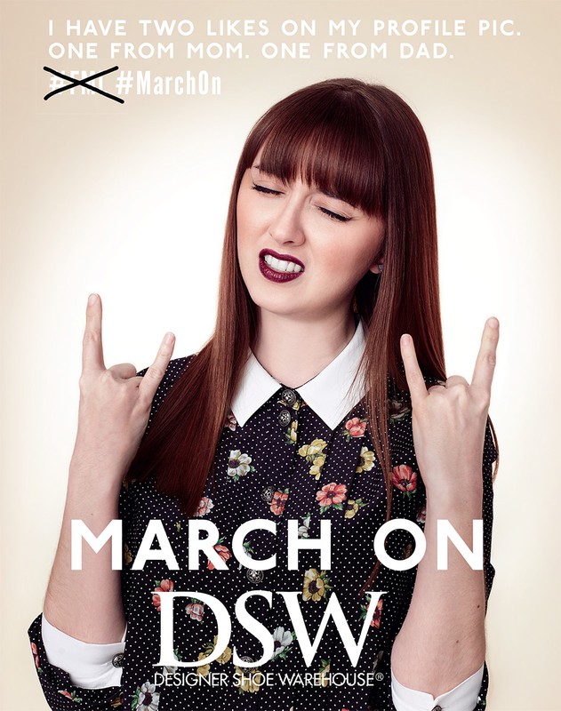 Young woman with bangs and dark lipstick wearing a floral dress with a white collar, making a rock and roll sign, against a tan background.