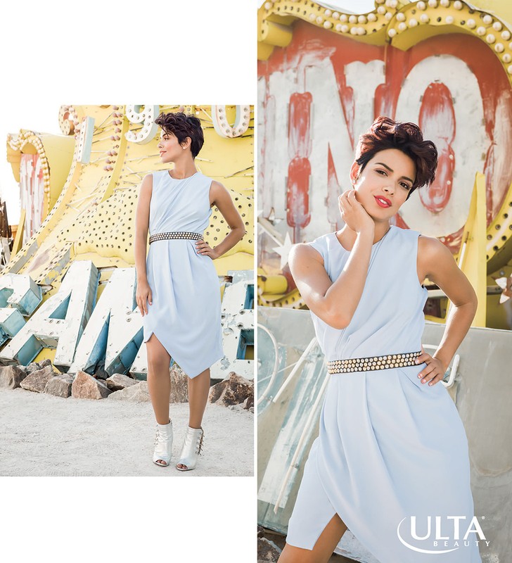 A young woman poses in a light blue dress with a decorative belt, next to a vintage Las Vegas sign with an Ulta Beauty logo overlay.