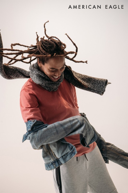 Smiling Black man in motion with dreadlocks and a scarf in a casual setting, showcasing a relaxed and carefree style for fashion.
