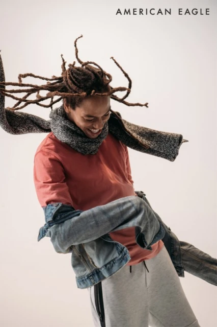 Smiling Black man in motion with dreadlocks and a scarf in a casual setting, showcasing a relaxed and carefree style for fashion.