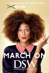 Close-up portrait of a woman with voluminous curly hair, freckles, and a pink-collared dark shirt against a warm gradient background.