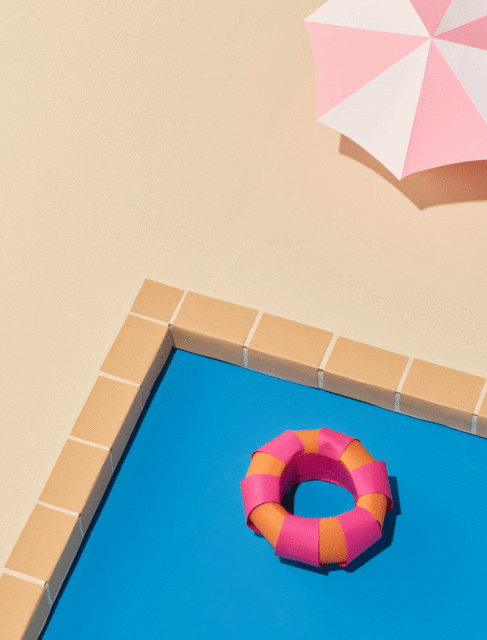 Top-down view of a blue swimming pool with a pink and orange striped inflatable ring and a pastel pink parasol with white stripes.