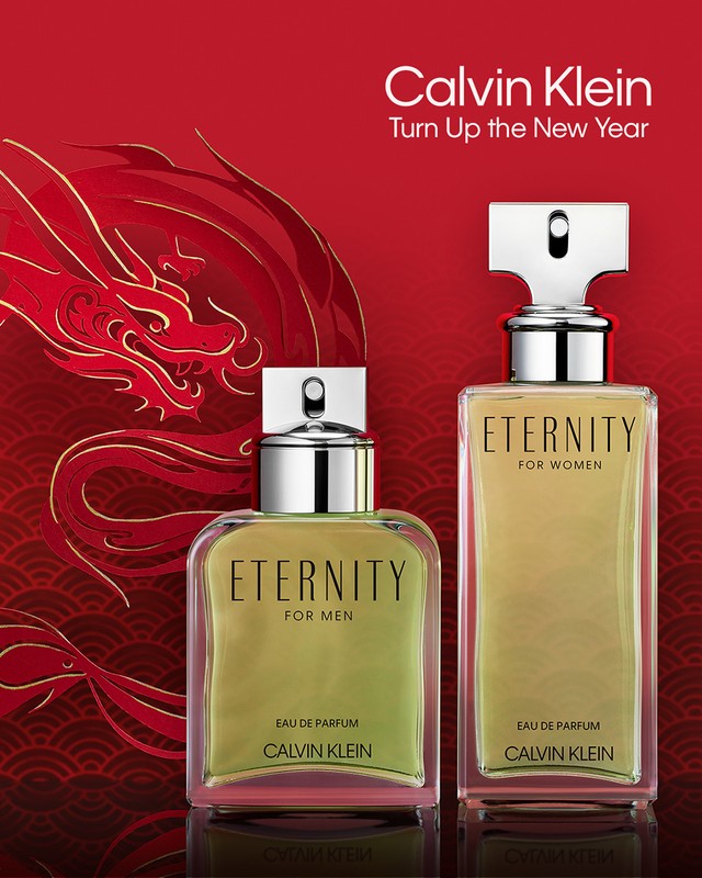 Two Eternity by Calvin Klein fragrance bottles, one for men and one for women, sit on a red surface with a golden dragon design.
