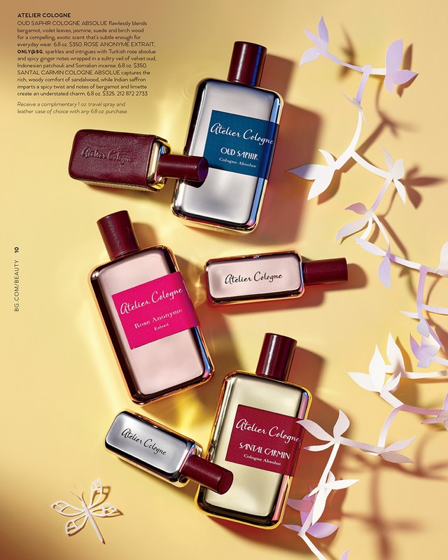 Atelier Cologne perfume bottles in a minimalist flat lay with maroon accents and decorative white paper sprigs on yellow backdrop.