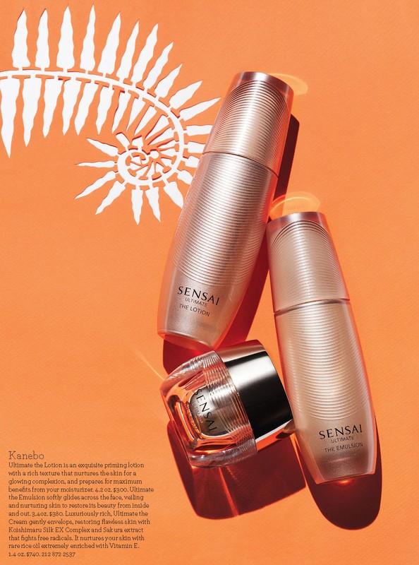 Beauty product flat lay featuring three beige Sensai Ultimate skincare bottles against a bright orange backdrop with decorative paper cut-out.