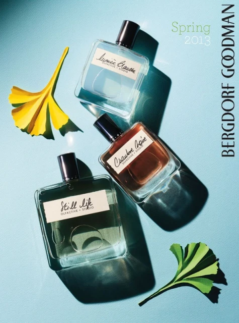 Three perfume bottles with brand labels and yellow ginkgo leaves, angled on a light blue surface with shadows, for Bergdorf Goodman.