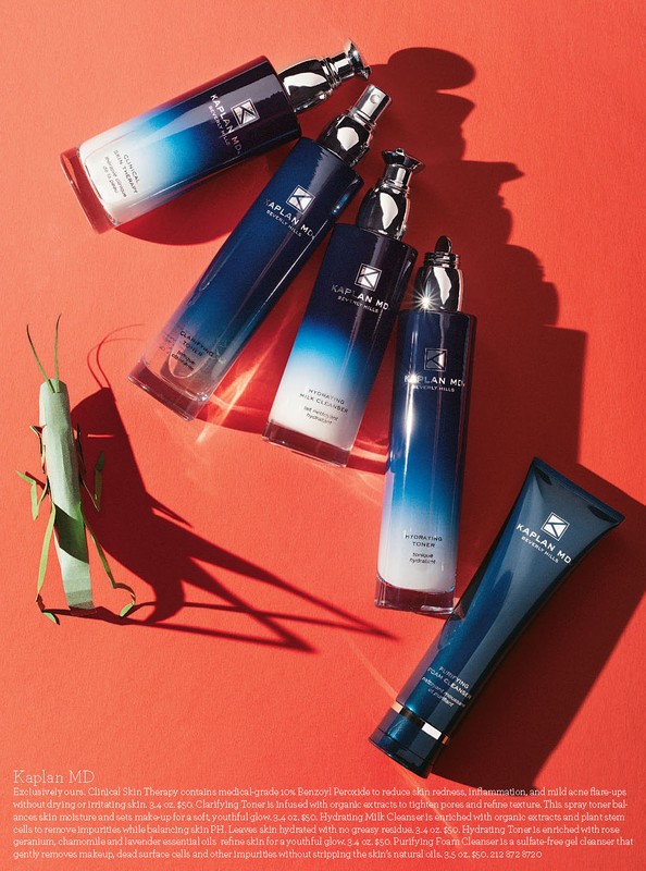 Kaplan MD skincare products in blue and white bottles arranged on a red surface with an insect, product-focused beauty photography.