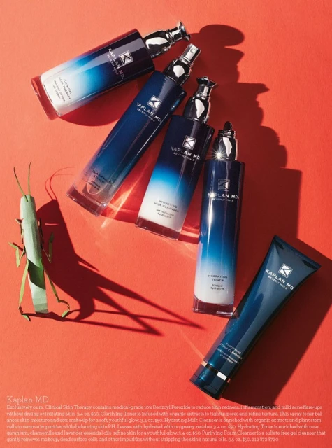 Kaplan MD skincare products in blue and white bottles arranged on a red surface with an insect, product-focused beauty photography.