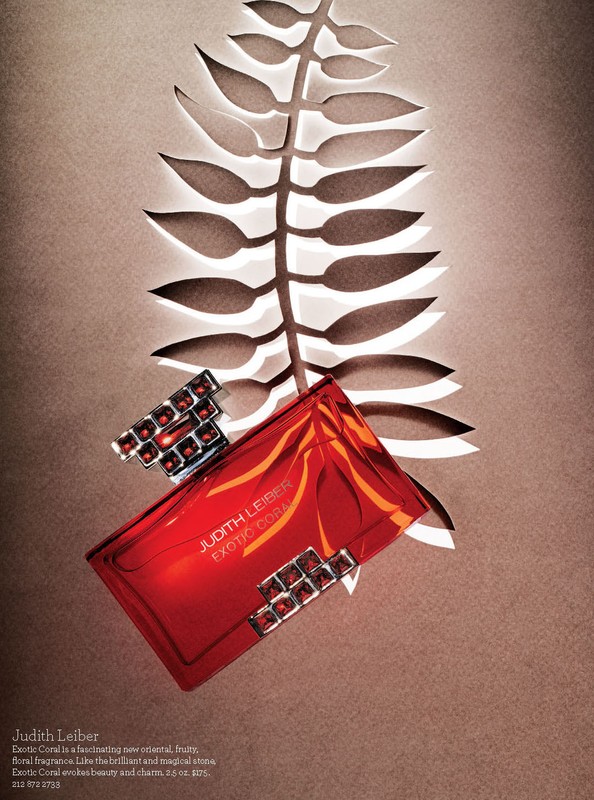 Judith Leiber Exotic Coral perfume bottle and jewelry displayed against a tan background with a white cut-paper fern design.
