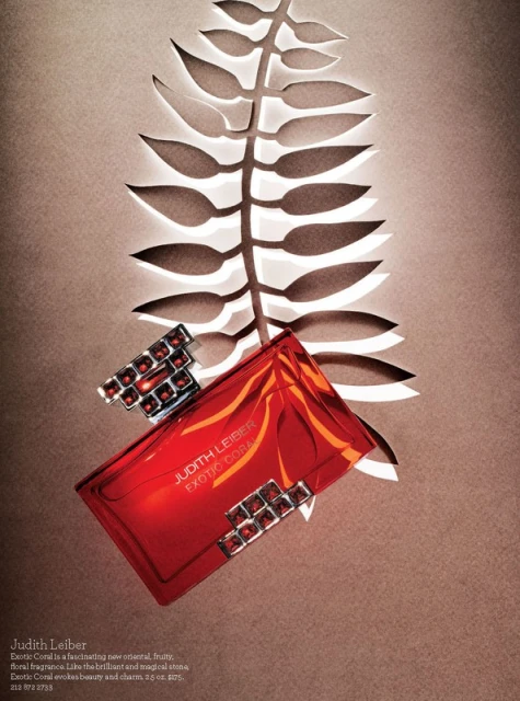 Judith Leiber Exotic Coral perfume bottle and jewelry displayed against a tan background with a white cut-paper fern design.