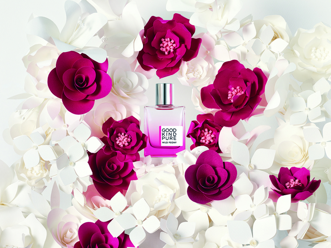 Rectangular perfume bottle displayed among magenta peony and white floral paper art elements against a white backdrop.