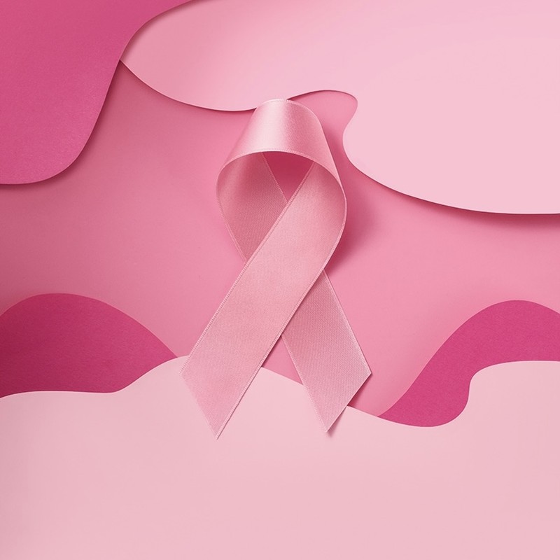 Close-up of a pink awareness ribbon on a pink layered background. Represents breast cancer awareness and support with its soft colors.