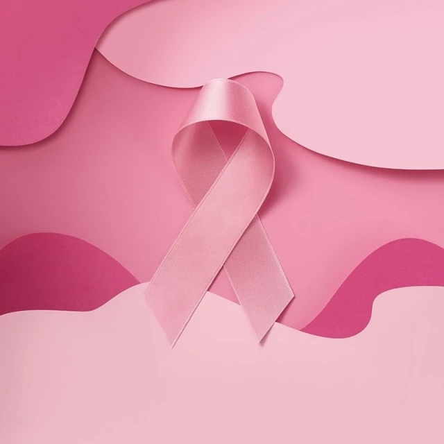 Close-up of a pink awareness ribbon on a pink layered background. Represents breast cancer awareness and support with its soft colors.