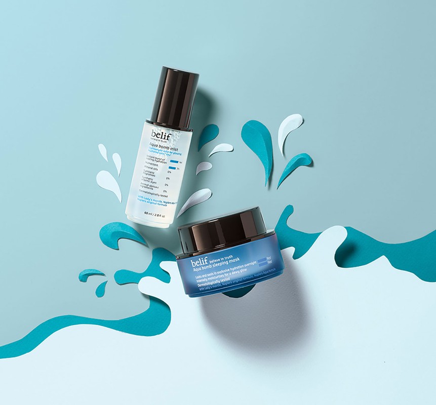 Belif skincare product bottles are displayed on a blue background with paper cutouts resembling water splashes and waves.