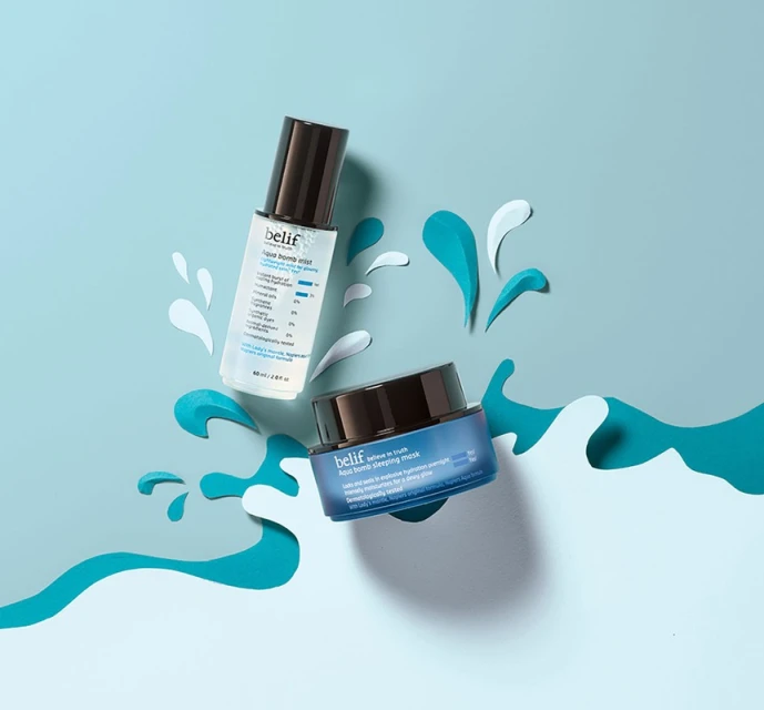 Belif skincare product bottles are displayed on a blue background with paper cutouts resembling water splashes and waves.