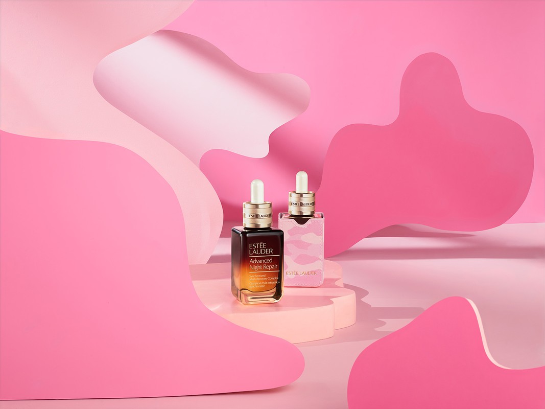 Still life studio shot of two Estee Lauder Advanced Night Repair serum bottles on pink pedestals against a cutout paper background.