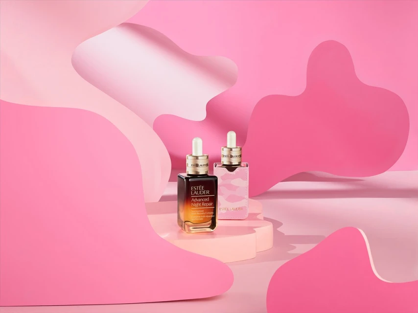 Still life studio shot of two Estee Lauder Advanced Night Repair serum bottles on pink pedestals against a cutout paper background.