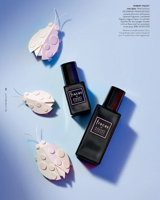 Two Fracas by Robert Piguet perfume bottles with black caps surrounded by decorative paper insect cutouts on a light blue backdrop.