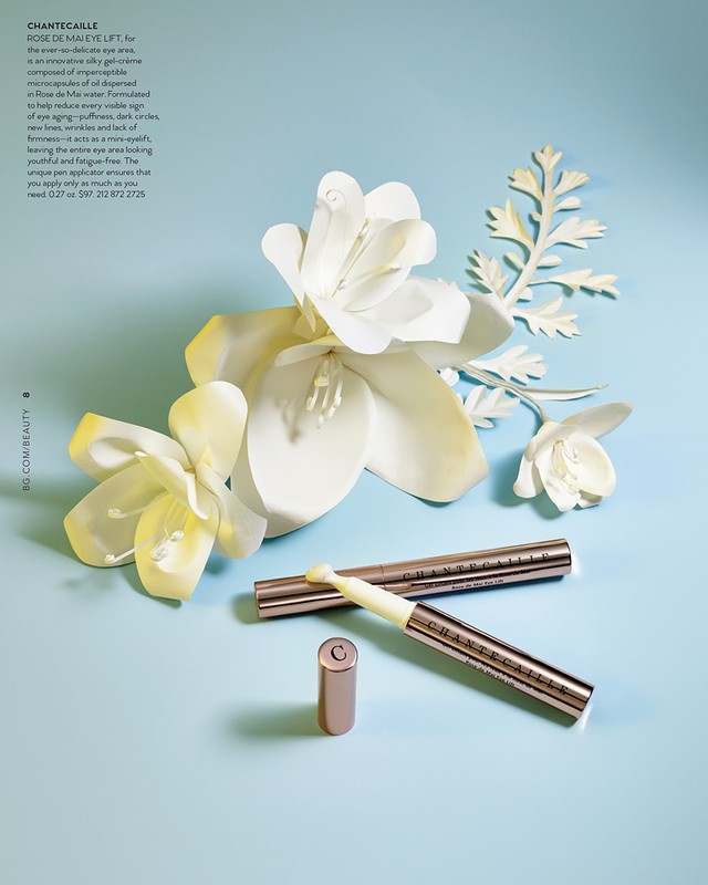Beauty still life: Chantecaille skincare products are arranged with white paper flowers on a light blue background, studio lighting.