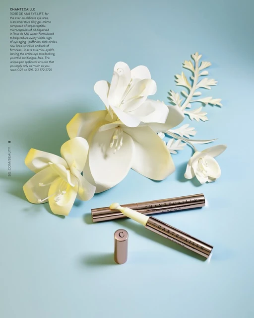 Beauty still life: Chantecaille skincare products are arranged with white paper flowers on a light blue background, studio lighting.