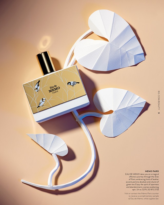Perfume bottle with gold accents and origami paper leaf decor on a pale background. Minimalist presentation for beauty and fragrance.