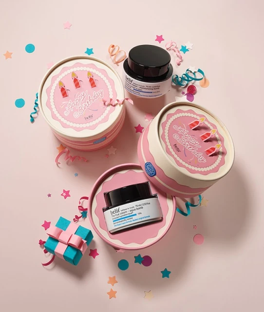 Belif skincare product assortment on a pink background with confetti and a wrapped gift, in cake-themed packaging for a birthday promotion.