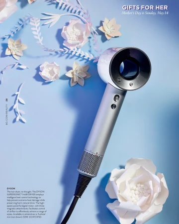 Studio shot of a Dyson Supersonic hair dryer against a light blue backdrop, accented with white paper flowers and leafy paper cutouts.