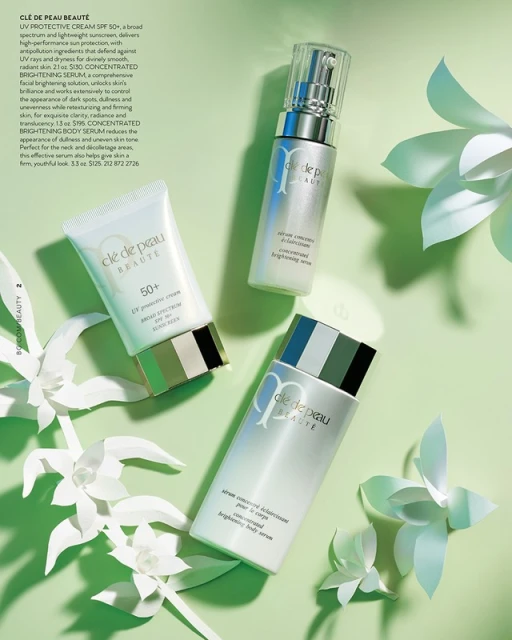 Three Cle de Peau Beaute skin care products, including UV protective cream and brightening serums, surrounded by white paper flowers on green.