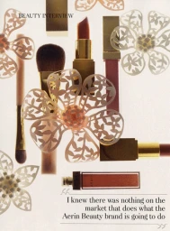 Flatlay of makeup products including lipstick tubes and makeup brushes arranged with paper flower cutouts on a white background
