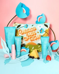 Tula Skincare product collection with tubes, a pouch, and paper crafted blue flowers against a pink and blue backdrop.