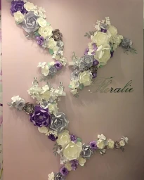 Elaborate paper floral installation in purple, white, and grey mounted on a pale pink wall with the word Floralie in script.