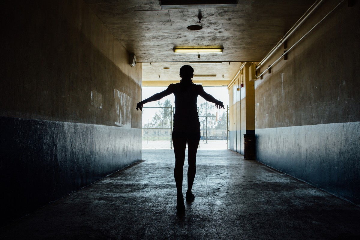 Silhouette of a person walking through a tunnel with arms outstretched, walking towards a bright opening on a sunny day.