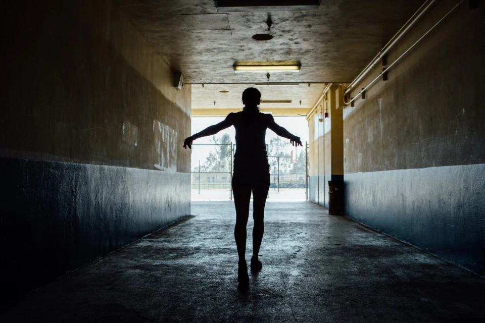 Silhouette of a person walking through a tunnel with arms outstretched, walking towards a bright opening on a sunny day.