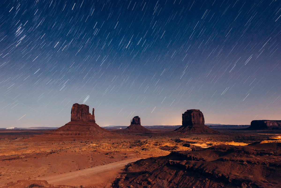 Dramatic long-exposure night landscape with star trails over Monument Valley, Arizona, featuring iconic sandstone buttes and mesas.